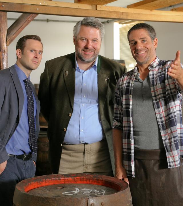 "Die Rosenheim-Cops - Der Letzte seiner Art": Die Kommissare König (Mark-Alexander Solf) und Stadler (Dieter Fischer) befinden sich in der Fass-Werkstatt mit dem Mitarbeiter Lennart Fritsch (Alex Huber). Dieser zeigt lachend nach vorne.