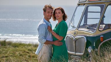 Nicolas (Max Woelky) und Olivia (Isabella Krieger) stehen im Dünengras am Meer und halten sich gegenseitig im Arm.