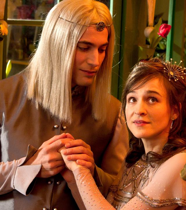 Der Mann im Mond hält die Hände von Siebenstein, die wie eine Prinzessin gekleidet ist und in den Nachthimmel schaut.