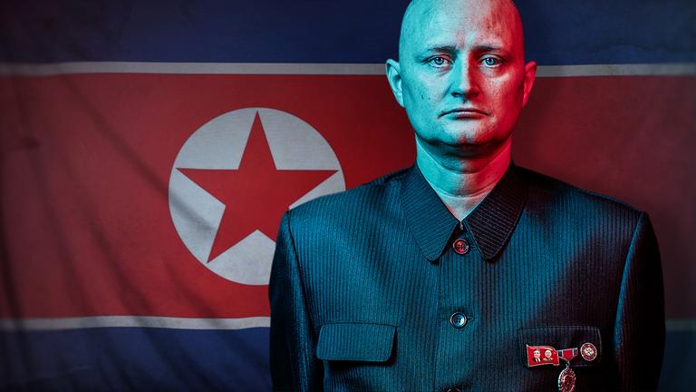 "The Mole - Infiltrating North Korea": Ein Mann in einer Uniform mit militärischen Abzeichen blickt ernst in die Kamera – im Hintergrund die nordkoreanische Flagge.