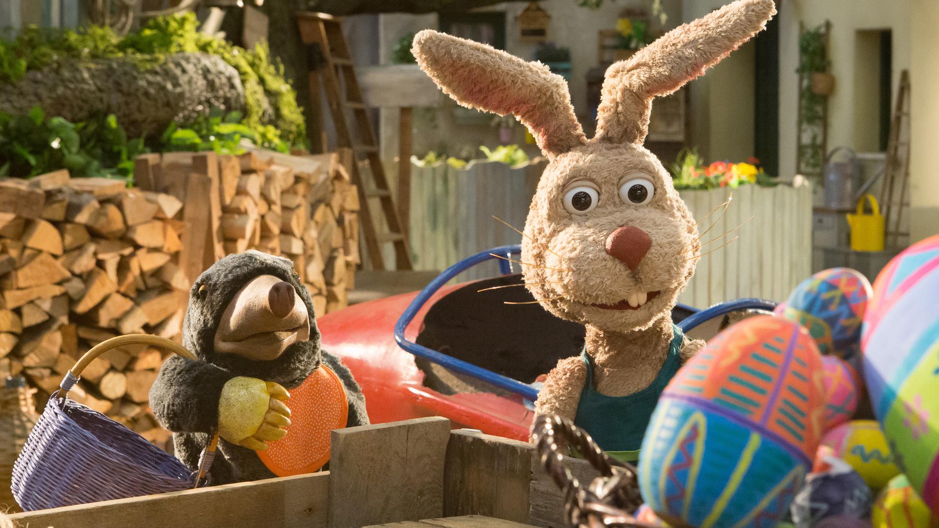 Grete, die ein Körbchen trägt, und Otto schauen erstaunt auf einen Korb voller bunter Ostereier.