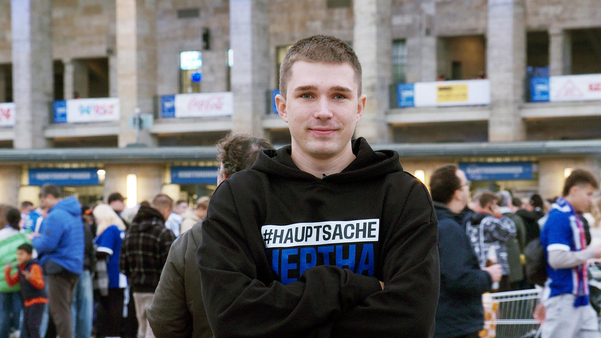Lächelnder junger Mann mit verschränkten Armen vor dem Berliner Olympia-Stadion.