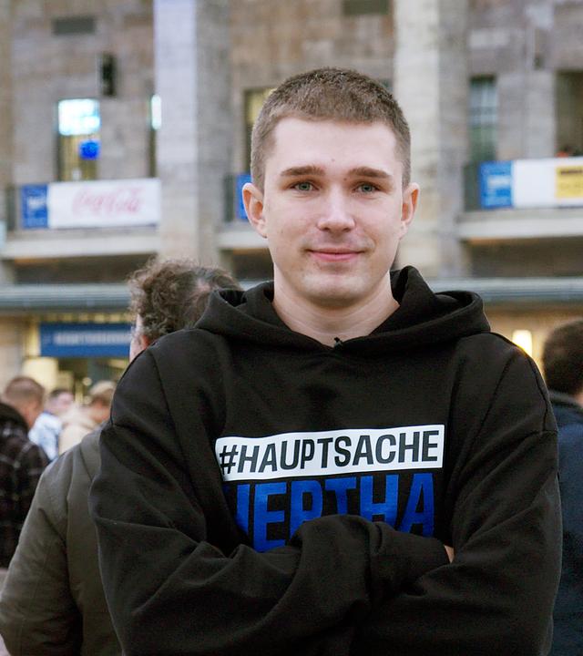 Lächelnder junger Mann mit verschränkten Armen vor dem Berliner Olympia-Stadion.