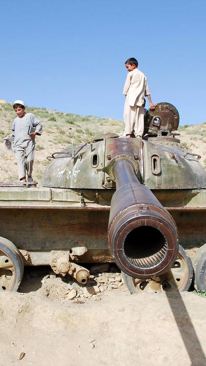 "Der Preis des Krieges - Afghanistan": In einer sandigen Landschaft stehen afghanische Kinder auf einem Militärpanzer, das Panzerrohr "zielt" Richtung Kamera.