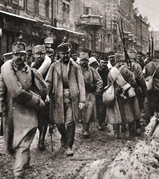 "Der Preis des Krieges - Erster Weltkrieg": Schwarz-Weiß-Fotoaufnahme mit bewaffneten Soldaten marschierend auf einer Straße. Einige blicken nach vorne, andere kehren dem Betrachter den Rücken zu.