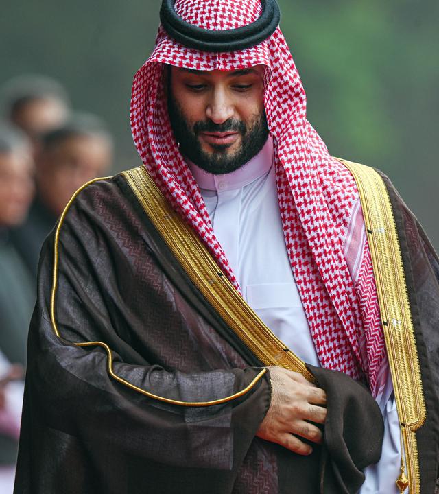 Mohammed Bin Salman mit saudischer Kopfbedeckung läuft an Menschenreihe vorbei und blickt halb nach unten.
