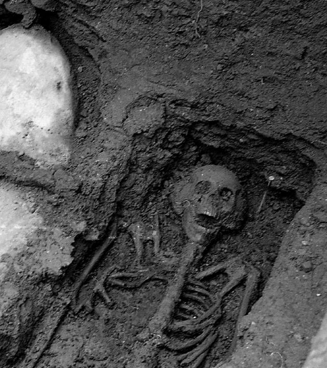 "Mysterien des Mittelalters - Der Ritter von St. Bees": Ein Skelett befindet sich freigelegt in einer Grube aus Erde. Daneben ist eine weitere Grube, in der ein in Leinen eingewickelter Körper liegt.