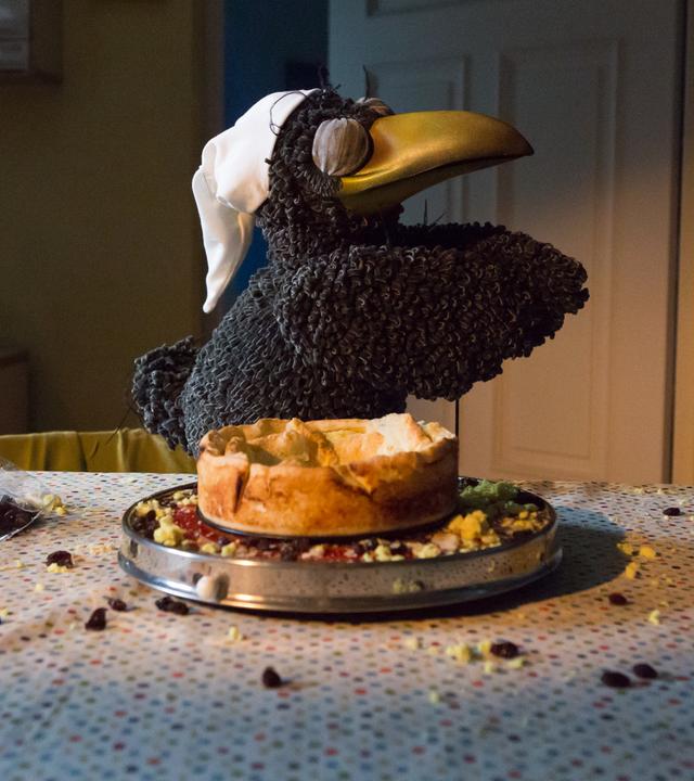 Rudi "schlafwandert" mit geschlossenen Augen und einer Schlafmütze auf dem Kopf neben einem angeknabberten Käsekuchen. Daneben liegen Krümel und Rosinen auf dem Tisch verteilt.