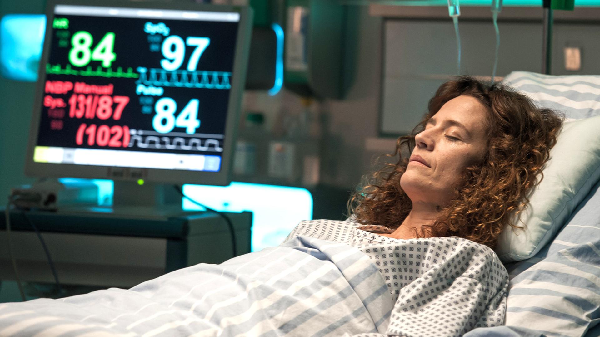 "Der Bergdoktor - Der schlimmste Schmerz": Rike Jäger (Regula Grauwiller) liegt mit geschlossenen Augen im Krankenbett und ist an diverse Apparaturen angeschlossen.