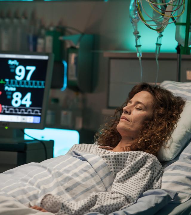 "Der Bergdoktor - Der schlimmste Schmerz (2)": Rike Jäger (Regula Grauwiller) liegt mit geschlossenen Augen im Krankenbett und ist an diverse Apparaturen angeschlossen.