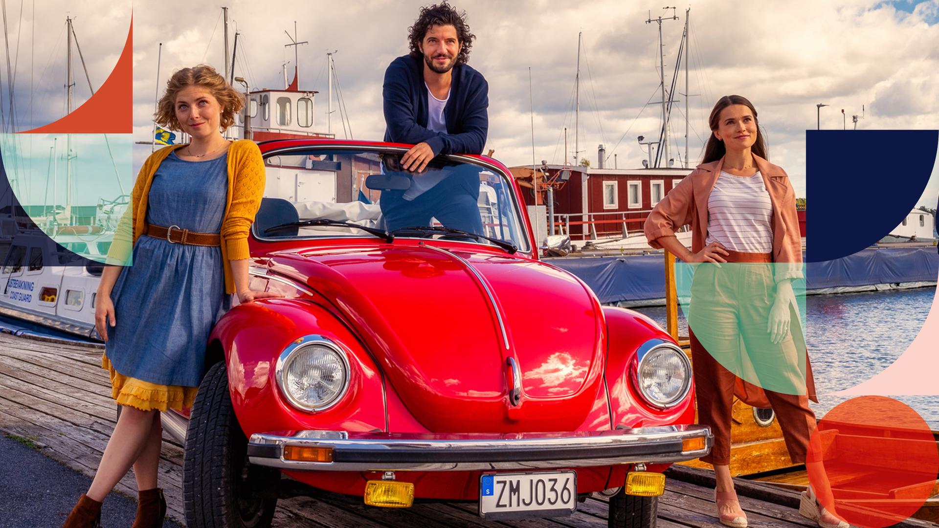 "Inga Lindström: Der schönste Ort der Welt": Noomi (Lilian Prent), Michel (Manuel Mairhofer), Maja (Zoe Moore) und Elias (Paul Triller) stehen am Hafen neben oder in einem roten Cabrio und blicken in die Kamera. Im Hintergrund Hafengebäude, Schiffe an Anlegerstellen, Gewässer, darüber blauer Himmel mit weißen Wolken.