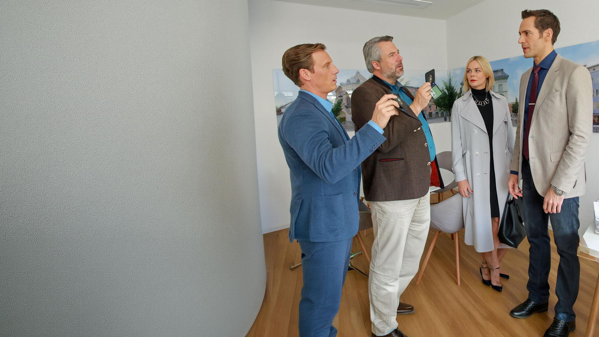 "Die Rosenheim-Cops - Der Tote im Garten": In einem Büro stehen die Kommissare Bach (Patrick Kalupa) und Stadler (Dieter Fischer) Barbara Quitt (Saskia Valencia) und Martin Bärlach (Alexander Mazza) gegenüber. Sie zeigen ihnen ihre Dienstmarke.