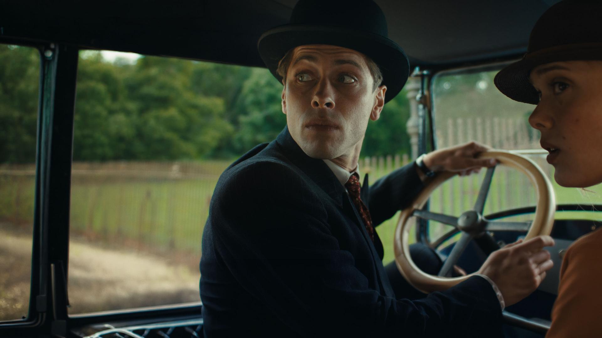 "This Is Not a Murder Mystery - Der Überlebende": René Magritte (Pierre Gervais) sitzt am Steuer eines Autos. Er trägt eine Melone auf dem Kopf. Neben ihm sitzt seine Frau Georgette (Mathilde Warnier), die nur halb im Profil zu sehen ist. Auch sie trägt einen Hut. Beide schauen über die Schulter nach hinten.