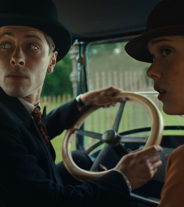 "This Is Not a Murder Mystery - Der Überlebende": René Magritte (Pierre Gervais) sitzt am Steuer eines Autos. Er trägt eine Melone auf dem Kopf. Neben ihm sitzt seine Frau Georgette (Mathilde Warnier), die nur halb im Profil zu sehen ist. Auch sie trägt einen Hut. Beide schauen über die Schulter nach hinten.