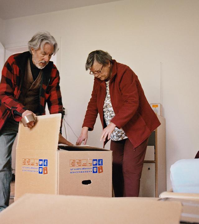 Zwei Männer stehen in einem Schlafzimmer und packen Umzugkartons