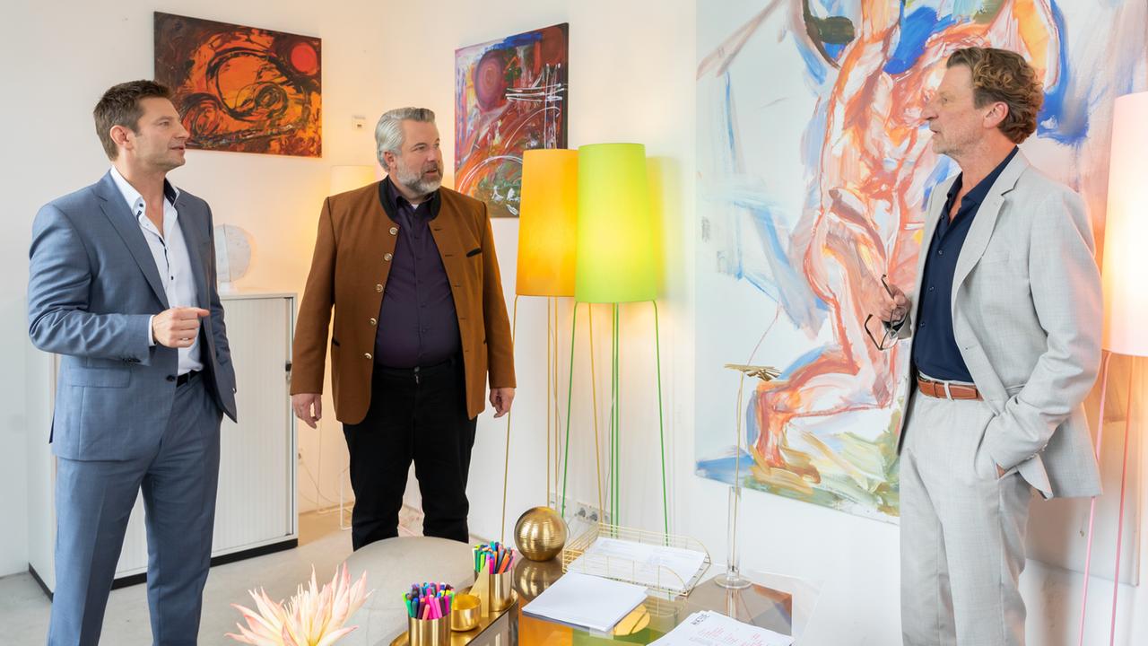 "Die Rosenheim-Cops - Der Unvollendete": Die Kommissare Hansen (Igor Jeftić) und Stadler (Dieter Fischer) stehen mit Professor Leonhard Bülow (Michael von Au) in dessen Zimmer und unterhalten sich. Im Hintergrund sind diverse moderne Gemälde zu sehen sowie zwei Stehlampen.