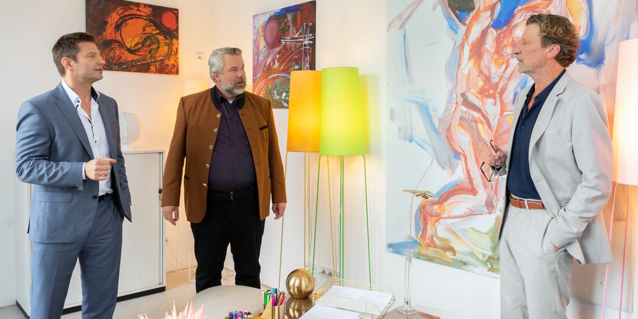 "Die Rosenheim-Cops - Der Unvollendete": Die Kommissare Hansen (Igor Jeftić) und Stadler (Dieter Fischer) stehen mit Professor Leonhard Bülow (Michael von Au) in dessen Zimmer und unterhalten sich. Im Hintergrund sind diverse moderne Gemälde zu sehen sowie zwei Stehlampen.