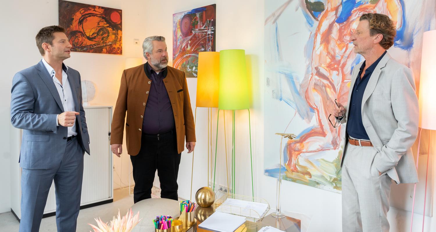 "Die Rosenheim-Cops - Der Unvollendete": Die Kommissare Hansen (Igor Jeftić) und Stadler (Dieter Fischer) stehen mit Professor Leonhard Bülow (Michael von Au) in dessen Zimmer und unterhalten sich. Im Hintergrund sind diverse moderne Gemälde zu sehen sowie zwei Stehlampen.