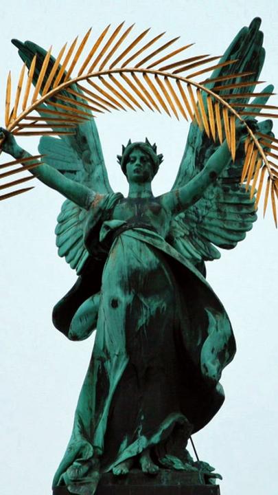 "Der vergiftete Frieden - Versailles und Europa": Statue des "Ruhms", mit Flügeln und hält einen goldenen Palmenkranz in die Höhe auf der Oper in Lwiw . Im Hintergrund weht die ukrainische Flagge.