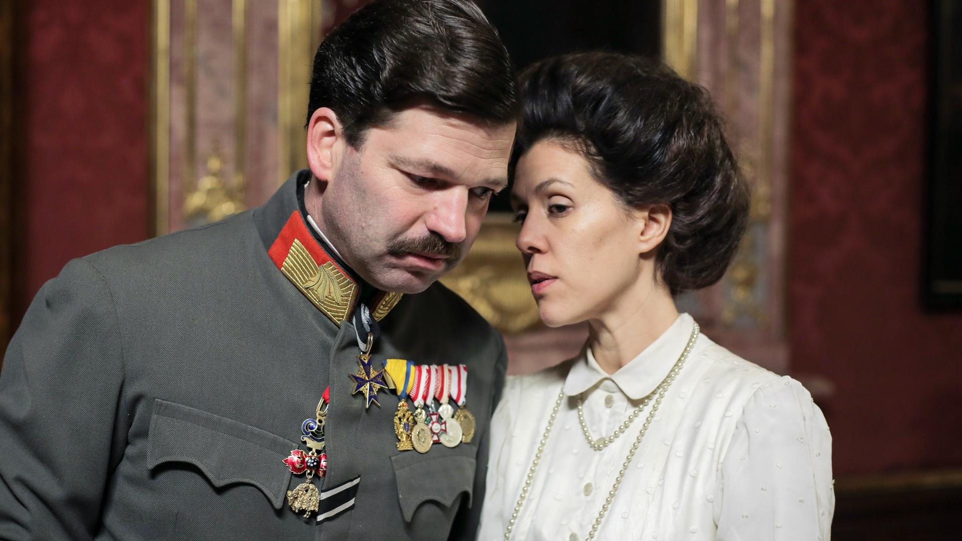 Ein Mann in Uniform steht neben einer Frau mit weisser Bluse.