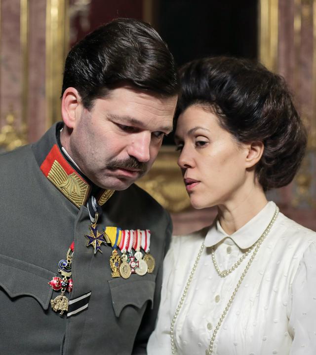 Ein Mann in Uniform steht neben einer Frau mit weisser Bluse.