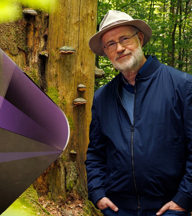 Harald Lesch im Nationalpark Bayerischer Wald vor einem Baum mit Schwammbewuchs.