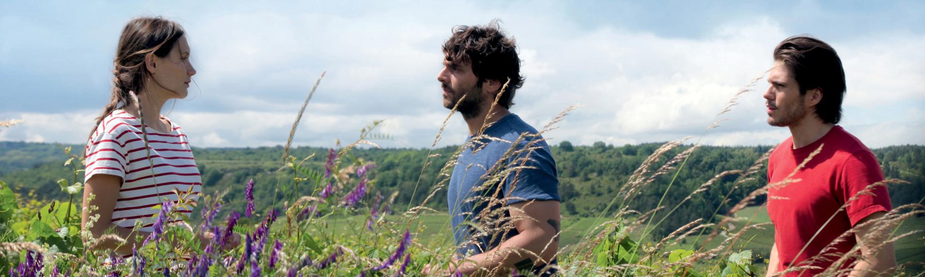 Die Geschwister Jean (Pio Marmaï), Juliette (Ana Girardot) und Jérémie (François Civil) stehen an ihrem Weinberg, zwischen blühenden Feldblumen.