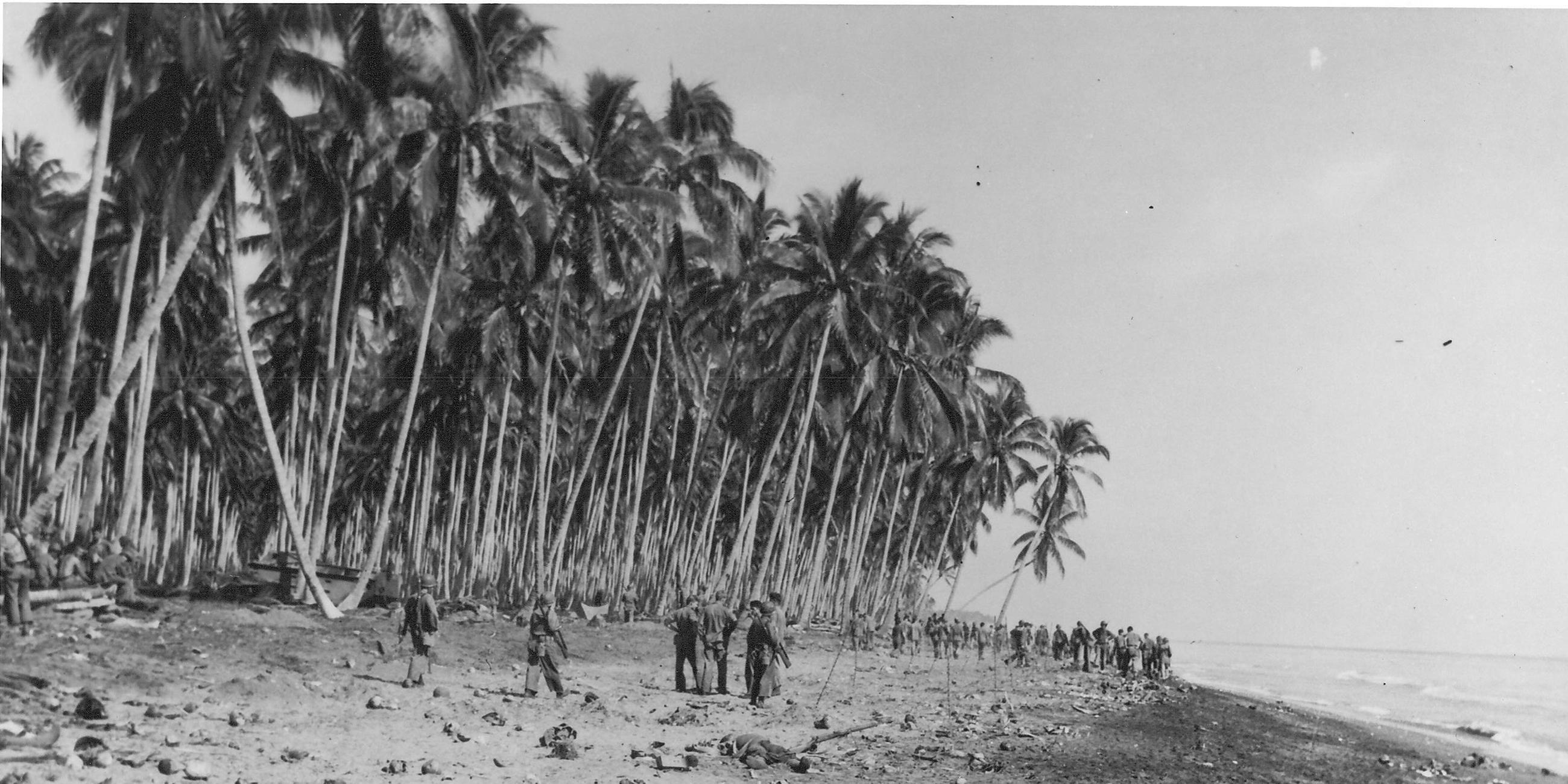 "Der Zweite Weltkrieg: An allen Fronten": Schwarz-Weiß-Aufnahme: Ein von Palmen gesäumter Strand nach der Schlacht. Gefallene liegen im Sand, im Hintergrund sind Überlebende zu sehen.