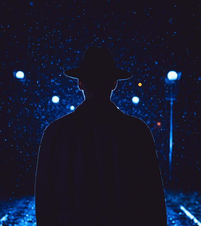 Ein Detektiv mit Hut und Regenjacke in der Nacht in einer verregneten Stadt