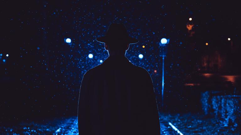 Ein Detektiv mit Hut und Regenjacke in der Nacht in einer verregneten Stadt