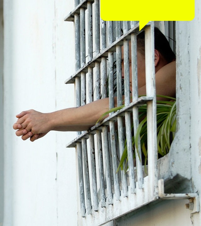 Eine inhaftierte Person lehnt sich aus einem vergittertem Fenster.