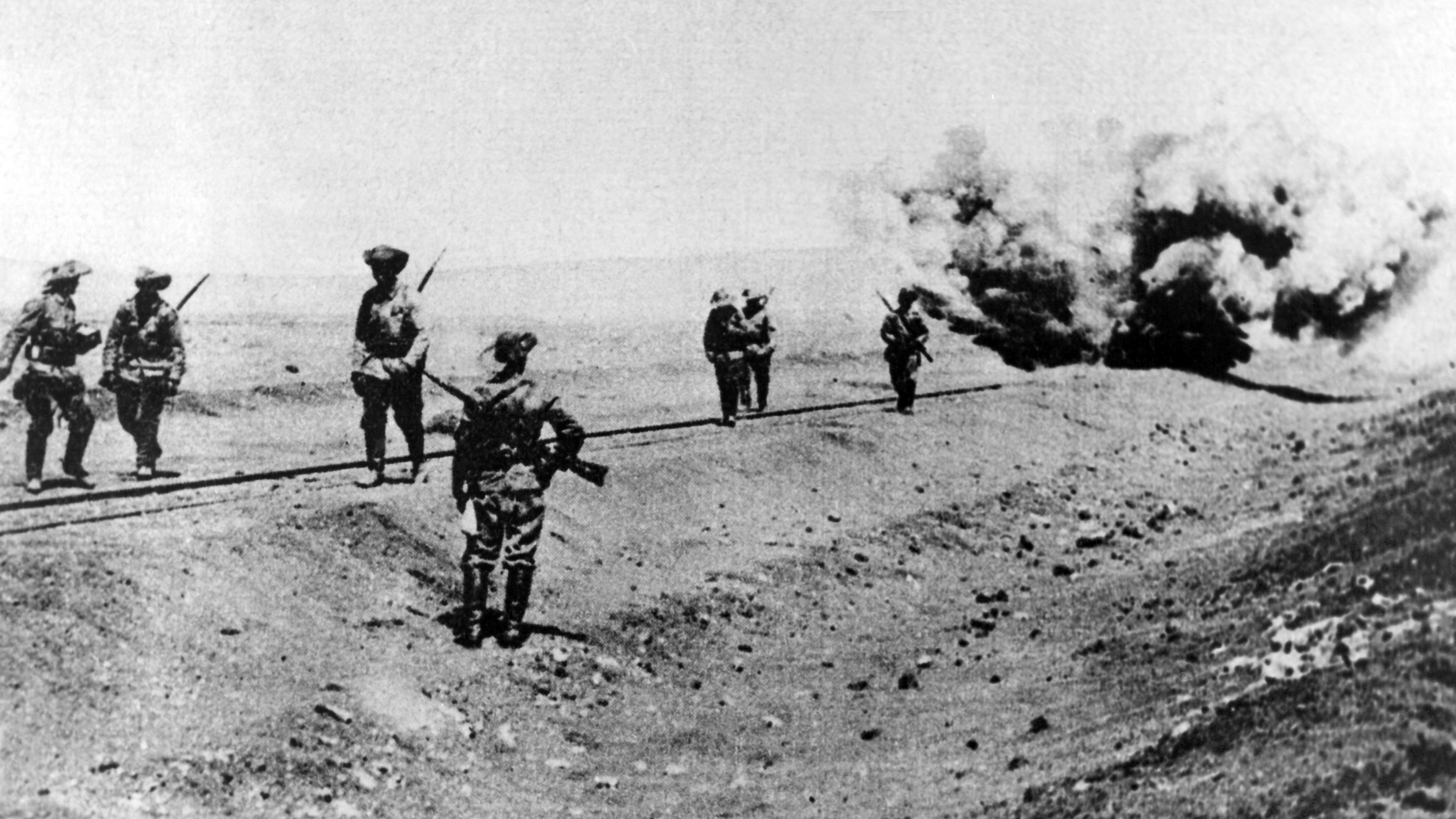 Deutsche Soldaten stehen im 1. Weltkrieg bei der Sprengung einer Eisenbahnlinie in der damaligen deutschen Kolonie Deutsch-Südwestafrika in einer Wüstenlandschaft.