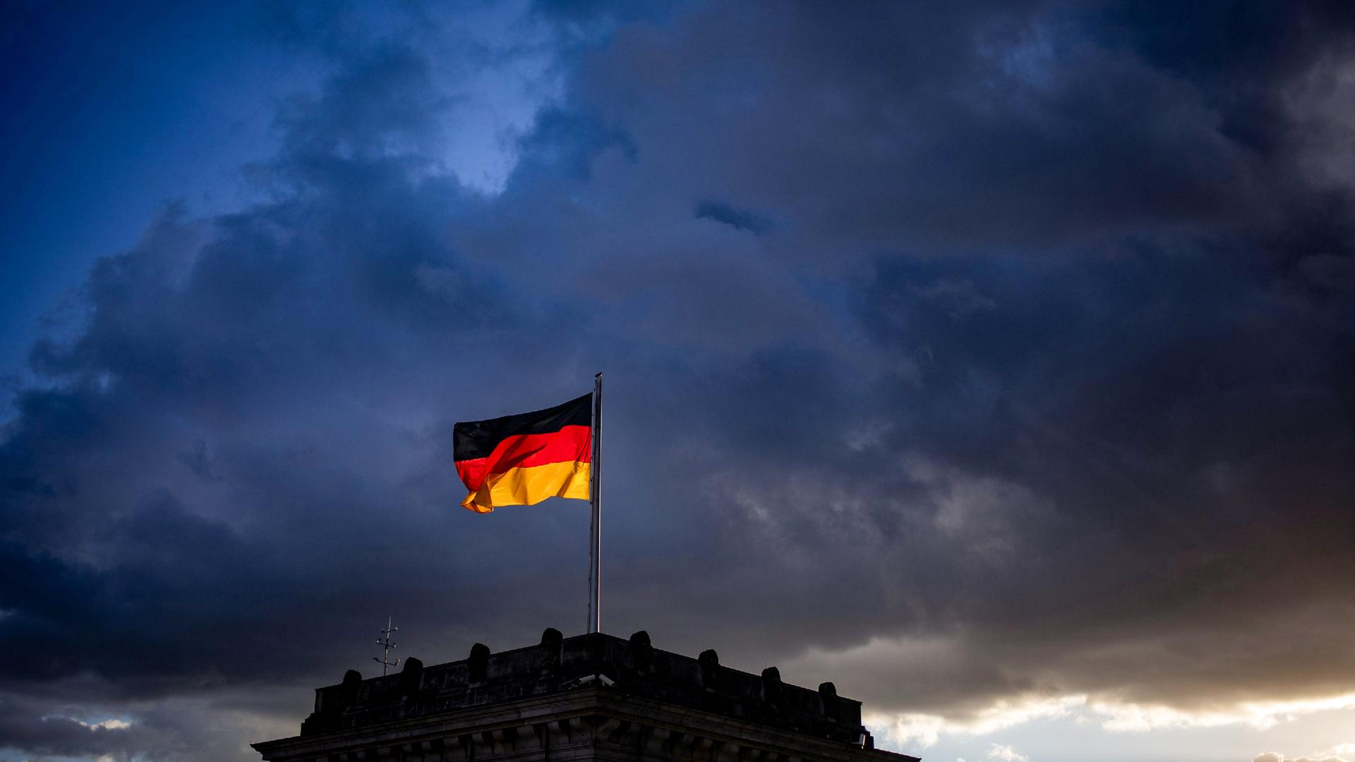 Die deutsche Flagge auf einem Gebäude vor dem Hintergrund dunkler Wolken.