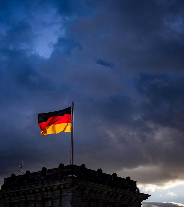 Die deutsche Flagge auf einem Gebäude vor dem Hintergrund dunkler Wolken.