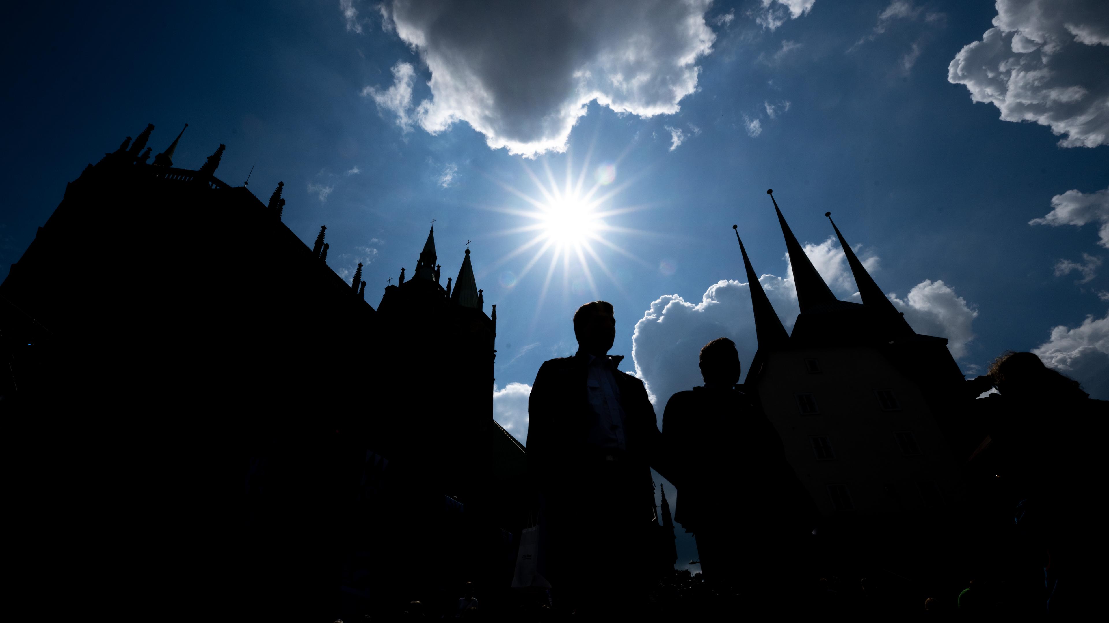 Besucher des Deutschen Katholikentages sind im Gegenlicht der Sonne vor der Silhouette des Doms zu sehen.
