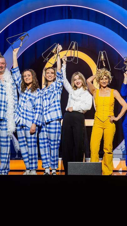 Es stehen zehn Personen auf einer Bühne. Der Hintergrund ist blau und gelb. Die Personen halten Trophäen in den Händen.
