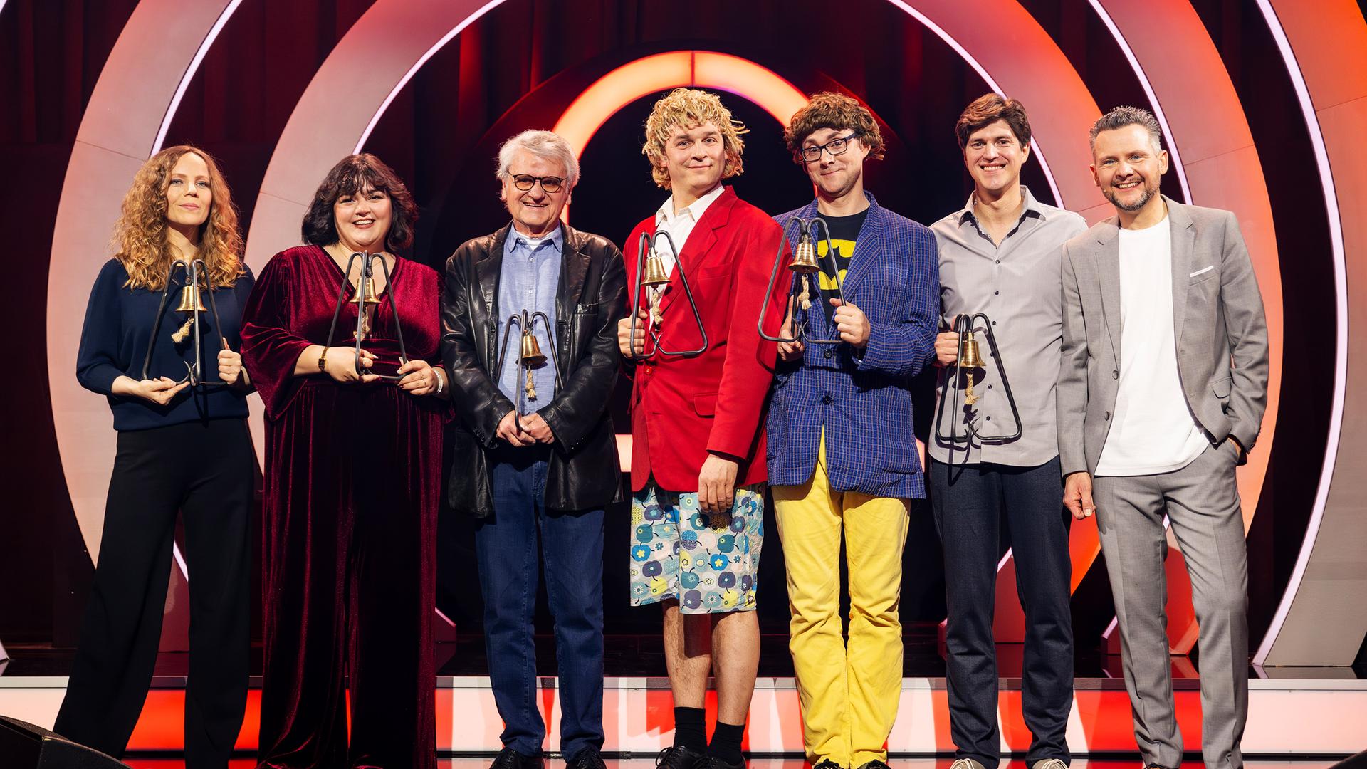 Es stehen sieben Personen auf einer Bühne. Der Hintergrund ist rot beleuchtet. Die Personen halten Trophäen in den Händen.