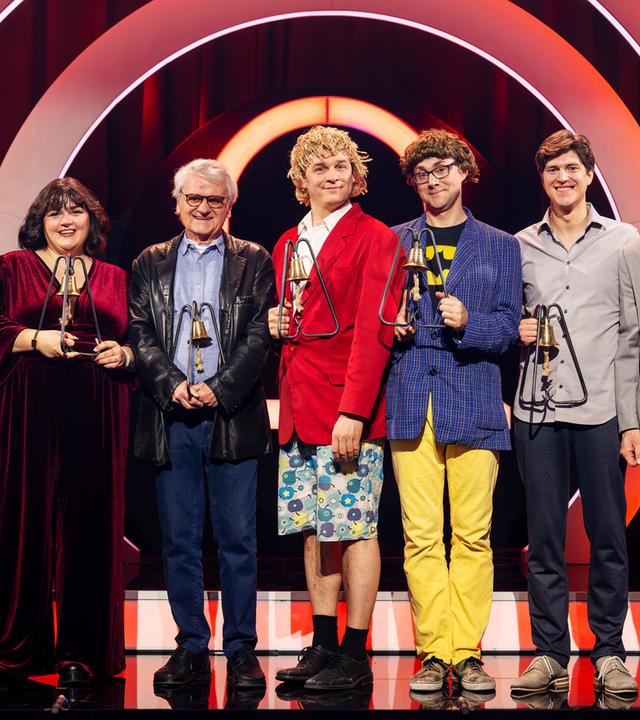 Es stehen sieben Personen auf einer Bühne. Der Hintergrund ist rot beleuchtet. Die Personen halten Trophäen in den Händen.