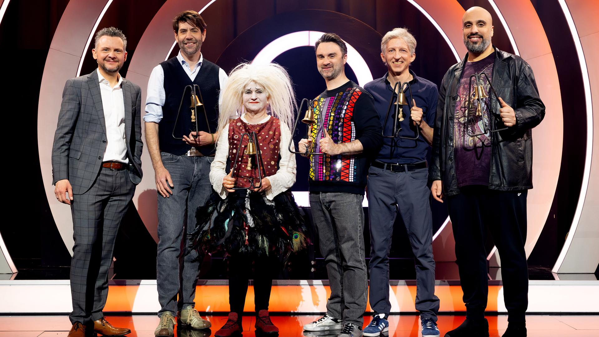 Es stehen sechs Personen auf einer Bühne. Der Hintergrund ist rot und weiß beleuchtet. Die Personen halten Trophäen in den Händen.