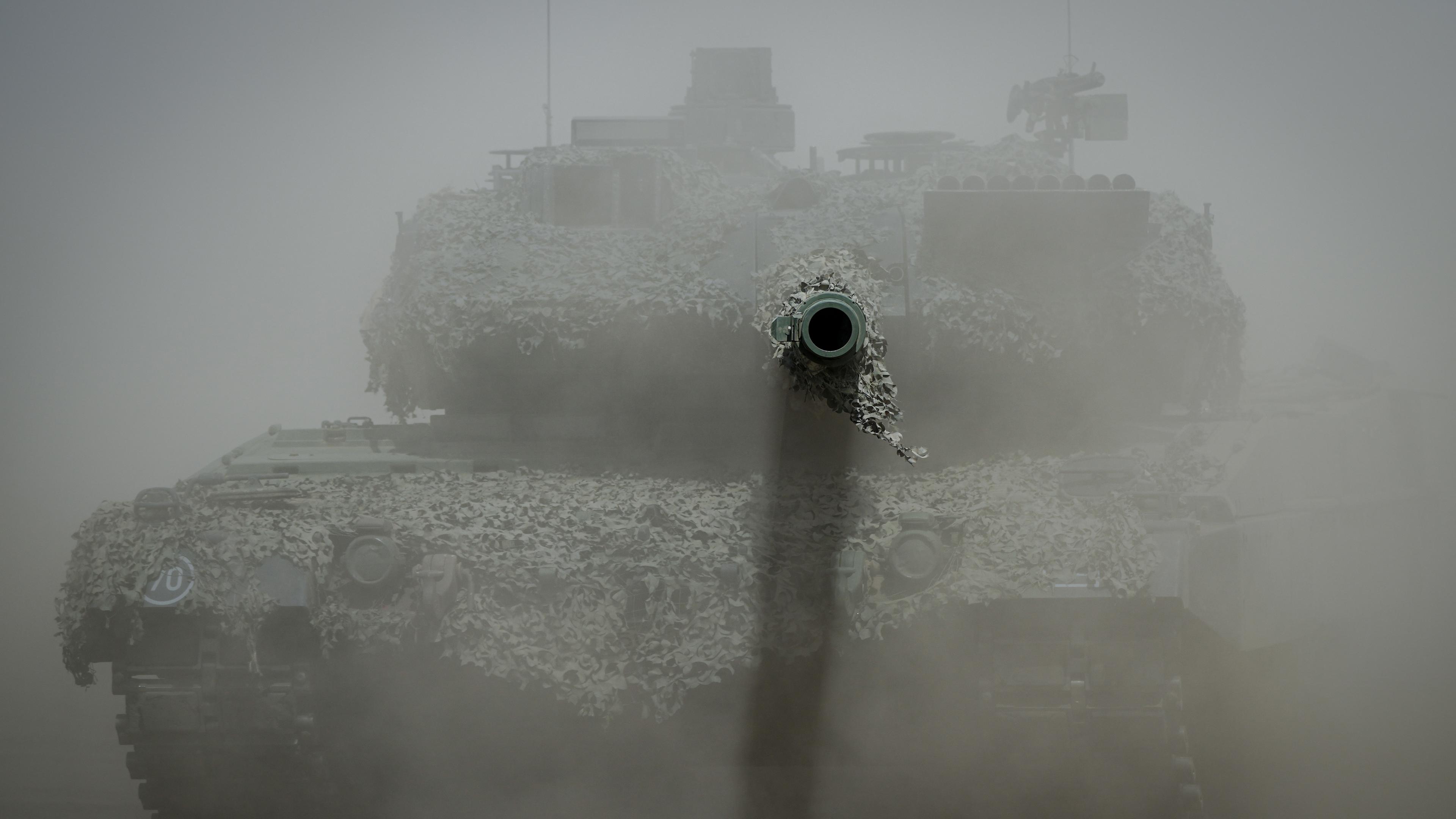 Ein Leopard 2 Kampfpanzer der Bundeswehr ist im Staub bei der Nato-Übung "Griffin Storm" zu sehen, das Kanonenrohr ragt aus der Staubwolke heraus.