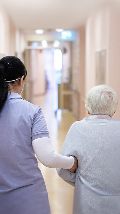 Pflegerin läuft mit älterer Frau einen Krankenhausgang entlang. Frankfurt, Hessen. 