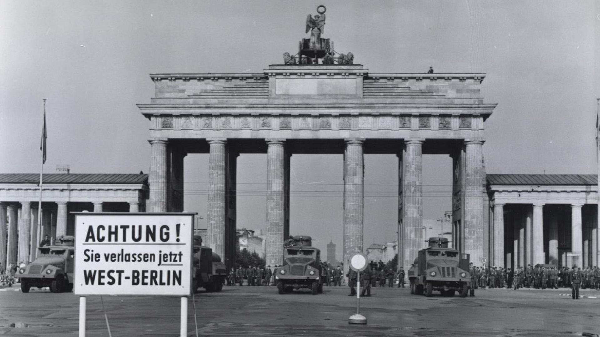 "Deutschland '61 - Countdown zum Mauerbau": Schwarz-Weiß-Bild vom Brandenburger Tor in Berlin. Vor dem Tor stehen vier gepanzerte Fahrzeuge und viele Soldaten. Davor ein Schild mit der Aufschrift "Achtung! Sie verlassen jetzt West-Berlin".
