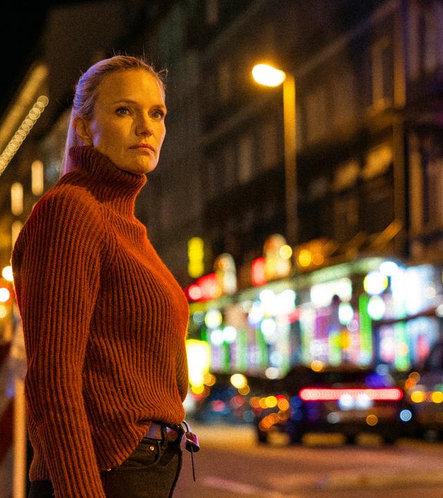 Sarah Tacke steht vor der Kulisse eines Rotlichtviertels irgendwo in Deutschland.