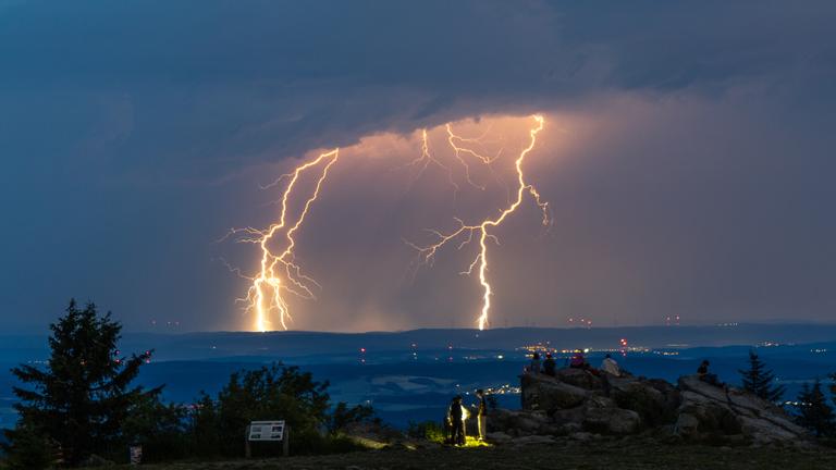 19.06.2026, Hessen, Schmitten: Menschen beobachten Blitze eines Gewitters am Großen Feldberg im Taunus.