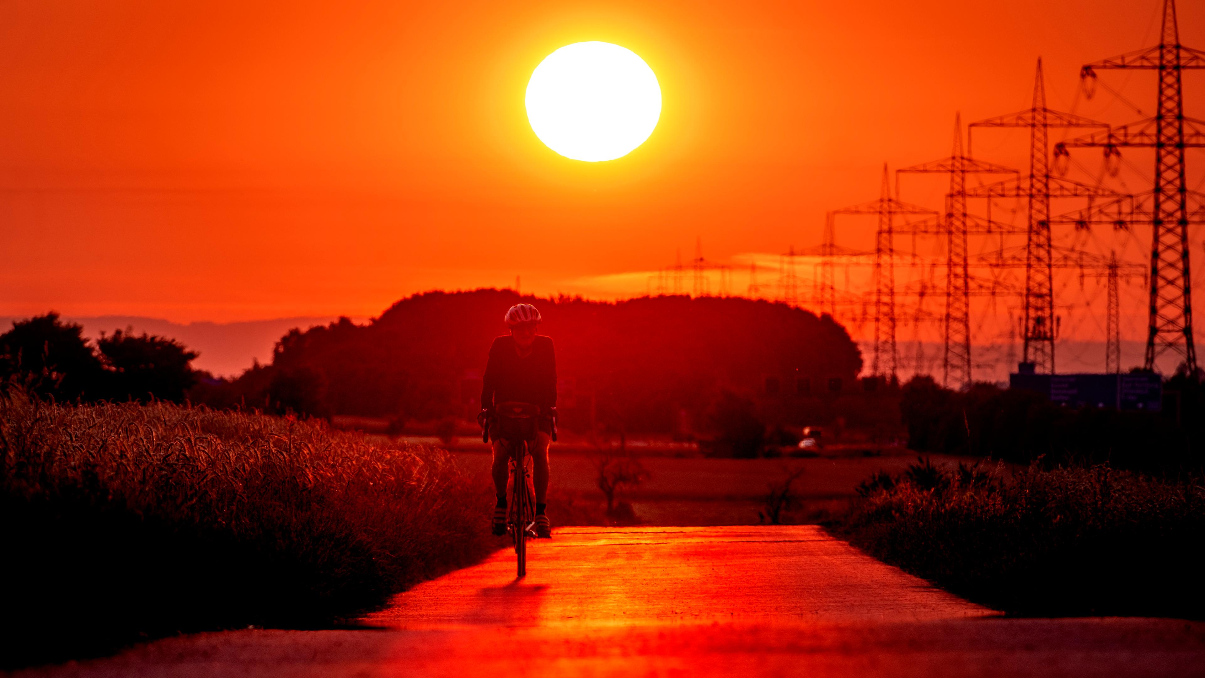 Ein Mann fährt bei Sonnenaufgang mit dem Fahrrad. Im Hintergrund scheint die Sonne.