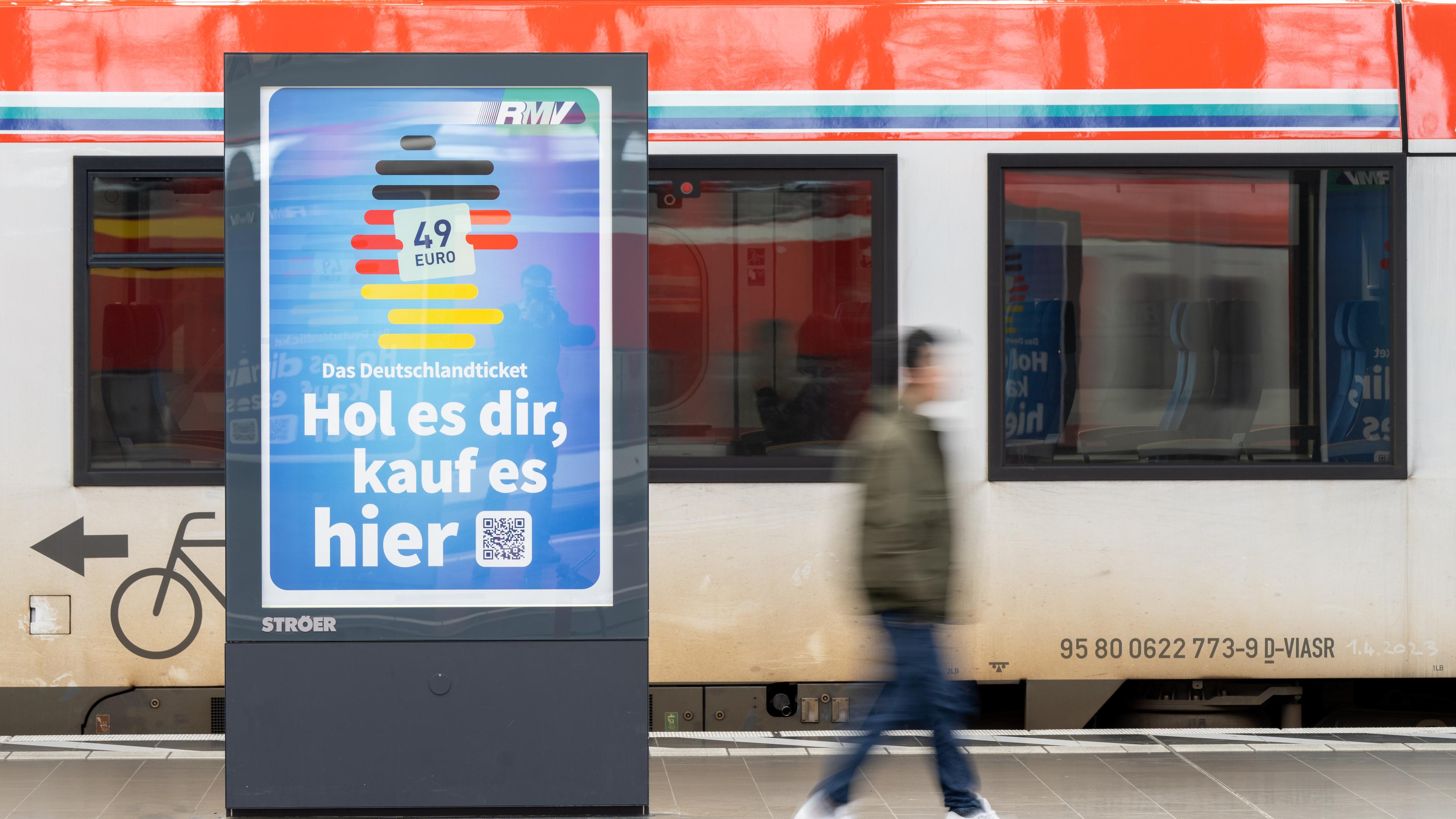 Auf einer digitalen Werbetafel an einem Bahngleis ist eine Werbung für das Deutschlandticket zu sehen. Darauf steht: "Das Deutschlandticket - hol es dir, kauf es hier".