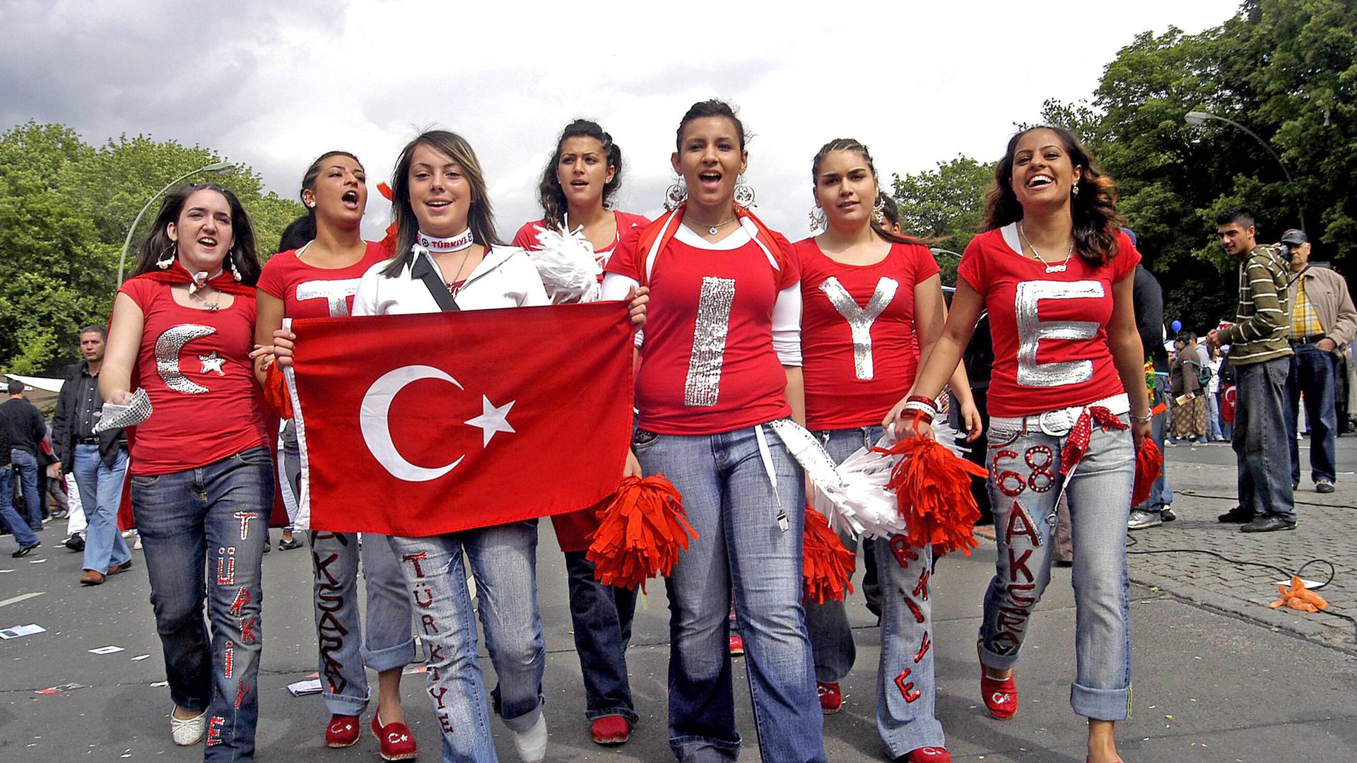 Eine Gruppe junger Frauen, auf deren roten T-Shirts Buchstaben stehen, die das Wort Türkiye ergeben, laufen mit einer türkischen Flagge auf einer Straße.