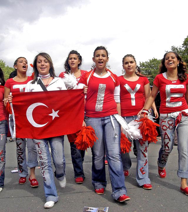 Eine Gruppe junger Frauen, auf deren roten T-Shirts Buchstaben stehen, die das Wort Türkiye ergeben, laufen mit einer türkischen Flagge auf einer Straße.