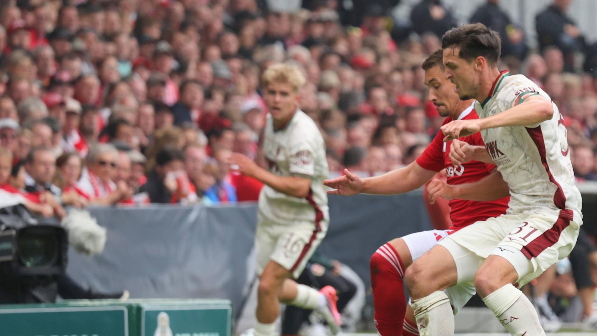Julian Guttau (Energie Cottbus, l.) und Keven Matteo Schlotterbeck (FC Augsburg) im Zweikampf am 22.08.2026 in Cottbus.