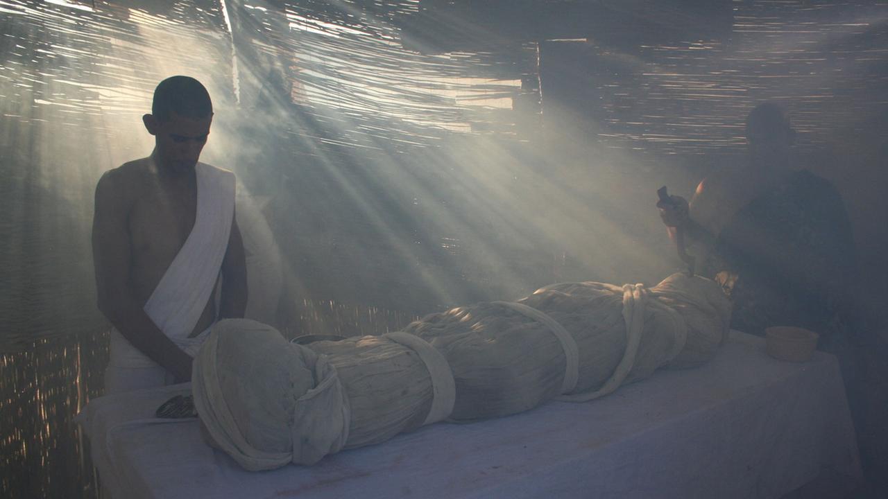 "Die Akte Tutanchamun": Zwei Männer stehen an einem Tisch, auf dem ein verhüllter Leichnam liegt.